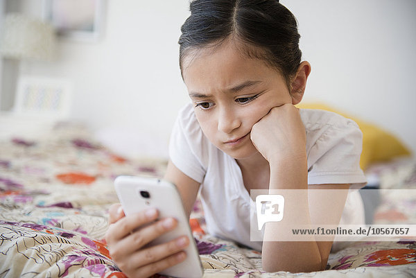Frustriertes Mädchen benutzt Mobiltelefon auf dem Bett