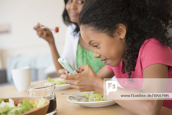 Mädchen benutzt Mobiltelefon beim Abendessen