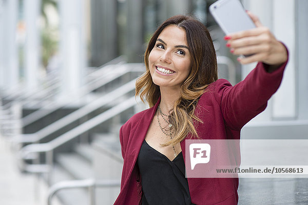 Hispanic businesswoman taking selfie outdoors