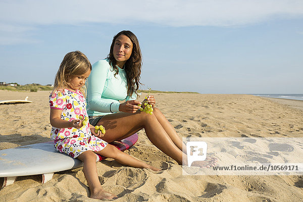 Mutter und Tochter essen Weintrauben am Strand