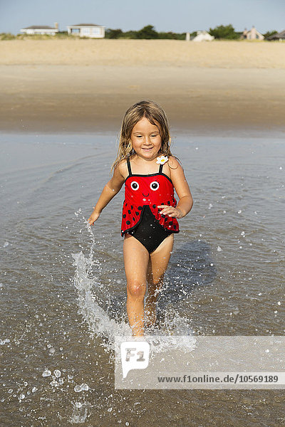 Gemischtrassiges Mädchen plantscht in den Wellen am Strand