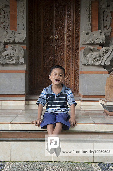 Asiatischer Junge sitzt vor einem verschnörkelten Gebäude