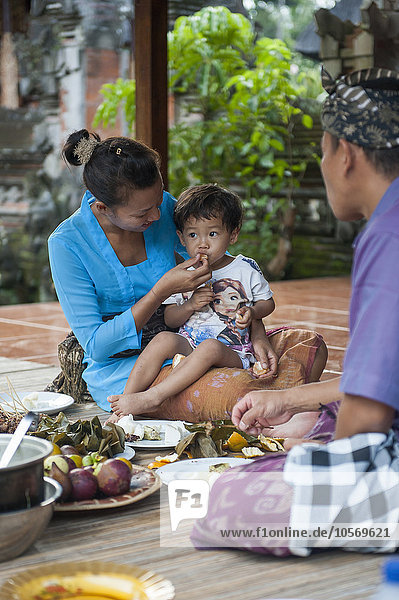 Asiatische Mutter füttert ihren Sohn auf einer gewebten Matte