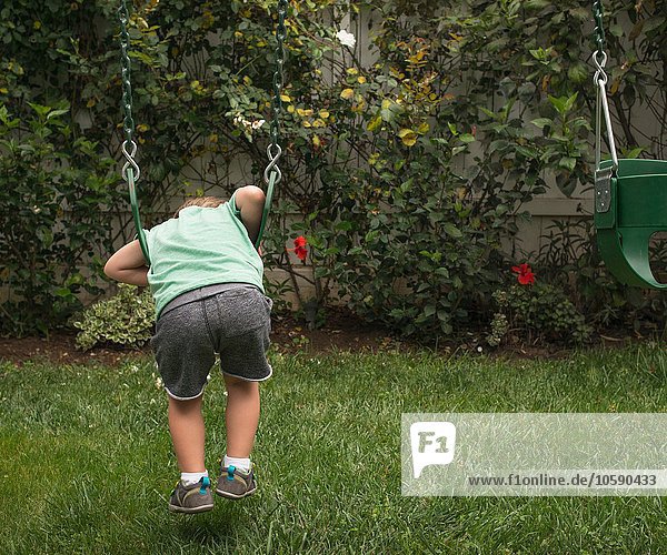Junge spielt auf der Gartenschaukel  Rückansicht