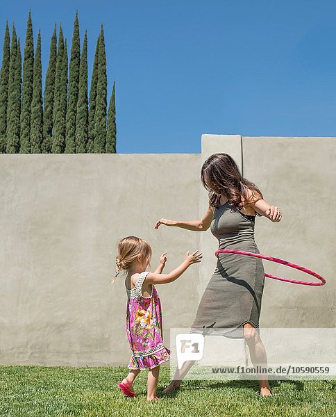 Mutter und Tochter spielen mit Kunststoffreifen im Garten