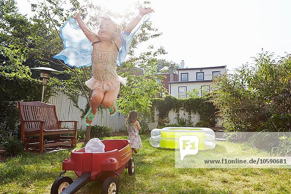 Mädchen in Schmetterlingskostüm springt vom Spielzeugwagen hoch
