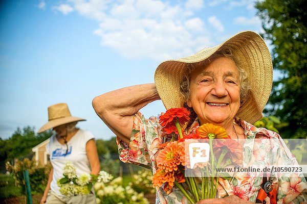 Senior woman holding onto straw hat and flowers on farm