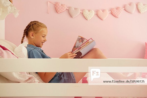 Seitenansicht des auf dem Bett sitzenden Mädchens Lesemagazin