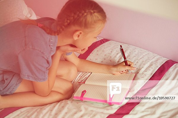 Hochwinkelansicht des knienden Mädchens auf dem Bett Schreiben im Notizbuch