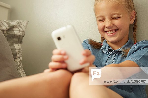 Mädchen sitzend an der Wand lehnend  Smartphone haltend  Augen geschlossen lächelnd
