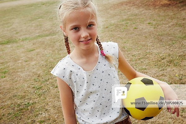 Hochwinkelansicht des Mädchens mit Zöpfen  die den Fußball halten und lächelnd in die Kamera schauen.