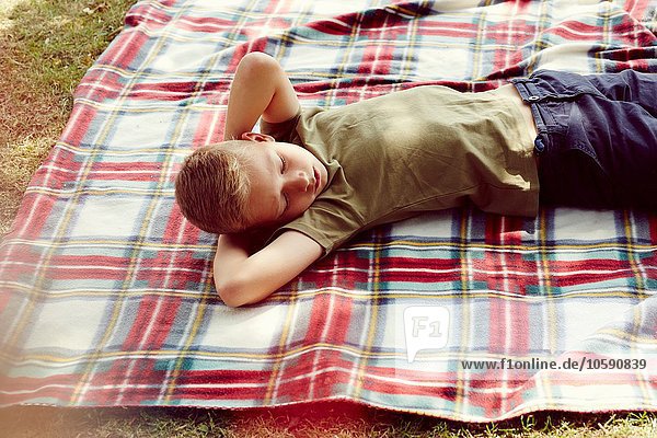 Hochwinkelansicht des Jungen auf Picknickdecke liegend Hände hinter dem Kopf wegblickend