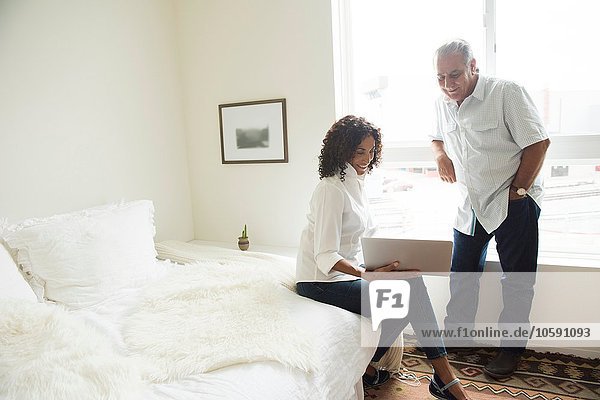 Senior man and wife looking at laptop in bedroom