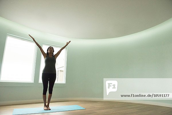 Mature woman practicing yoga with arms raised in curved room