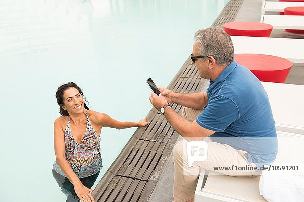 Senior Mann fotografiert Frau mit Smartphone am Pool