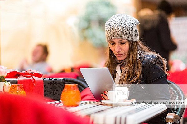 Reife Frau beim Durchstöbern des digitalen Tabletts im Straßencafé
