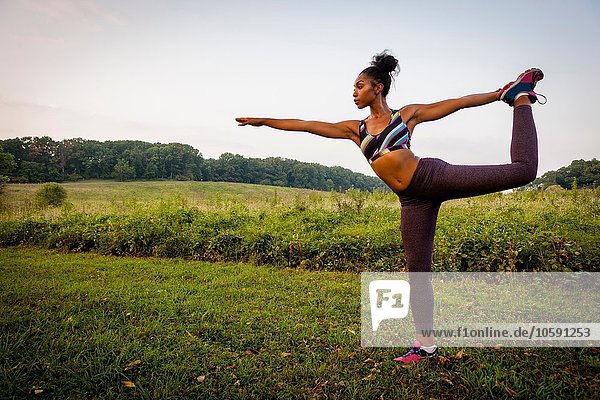 Junge Frau praktiziert Yoga-Pose im ländlichen Park