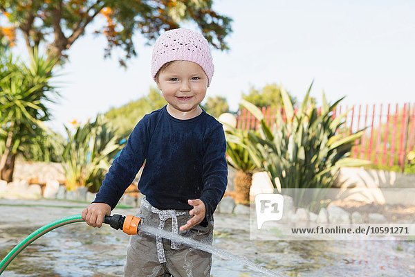 Kleinkind beim Spielen mit Wasserschlauch im Garten