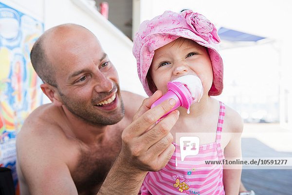 Father feeding toddler daughter ice cream cone on beach