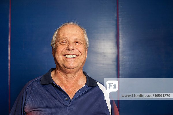 Portrait of senior man (table tennis player) wearing navy blue polo shirt looking at camera smiling