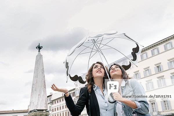 Lesbian couple holding umbrella checking for rain with hand  looking up  Piazza Santa Maria Novella  Florence  Tuscany  Italy