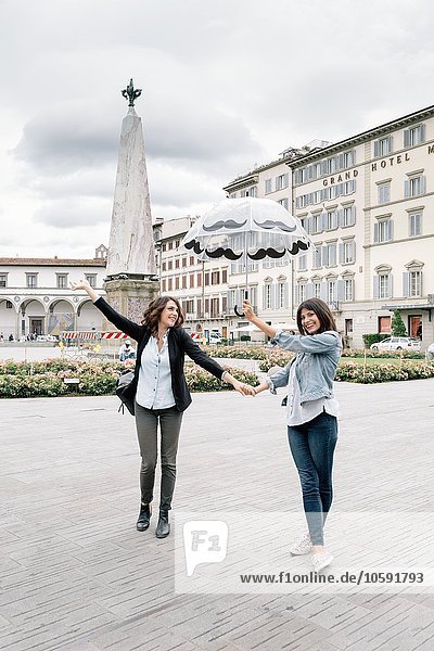 Lesbian couple holding umbrella fooling around holding hands smiling  Piazza Santa Maria Novella  Florence  Tuscany  Italy