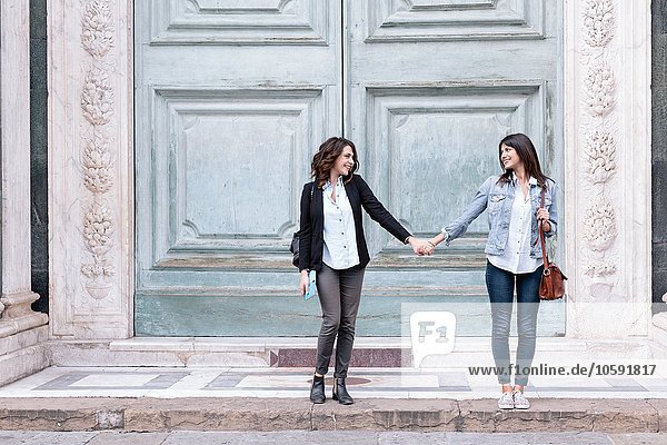 Lesbian couple standing in oversized church doorway holding hands  Piazza Santa Maria Novella  Florence  Tuscany  Italy