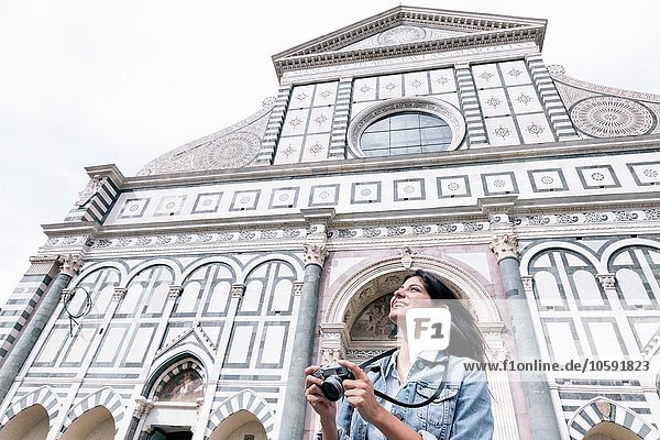 Low angle view of young woman using digital camera in front of church looking up  Piazza Santa Maria Novella  Florence  Tuscany  Italy