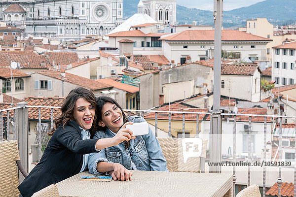 Lesbisches Ehepaar sitzt am Tisch auf der Dachterrasse und benutzt ein Smartphone  um das Lächeln des Selfie mitzunehmen  Florenz  Toskana  Italien