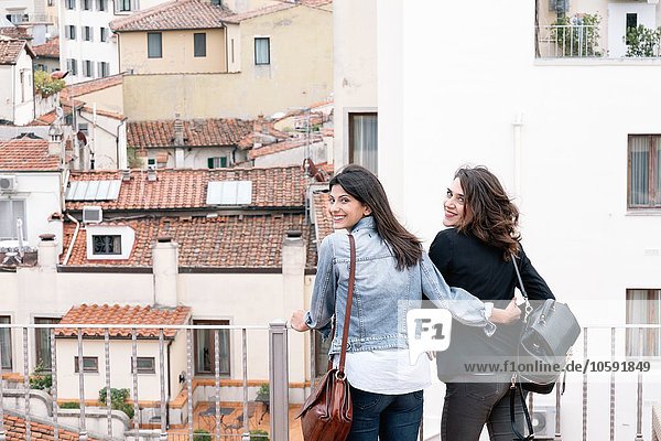 Rear view of lesbian couple standing of roof terrace looking over shoulder at camera smiling  Florence  Tuscany  Italy
