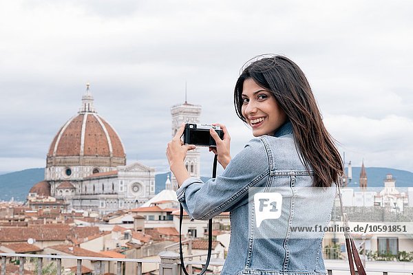 Young woman taking photo of Florence Cathedral and Giotto's Campanile looking over shoulder smiling  Florence  Tuscany  Italy