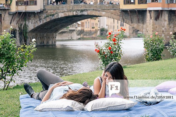 Lesbisches Paar liegt auf einer Decke vor der Ponte Vecchio über dem Fluss Arno  Florenz  Toskana  Italien