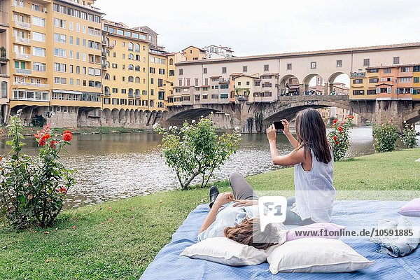 Lesbisches Paar auf Decke mit Digitalkamera  um Ponte Vecchio über dem Fluss Arno  Florenz  Toskana  Italien zu fotografieren.