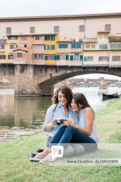 Lesbian couple sitting together looking at digital camera in front of Ponte Vecchio smiling  Florence  Tuscany  Italy