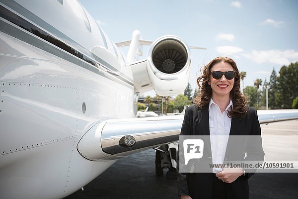 Portrait of mid adult female businesswoman and private jet at airport