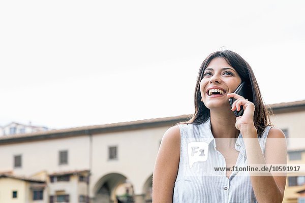 Blick auf eine junge Frau  die auf dem Handy lächelnd aufschaut  Florenz  Toskana  Italien