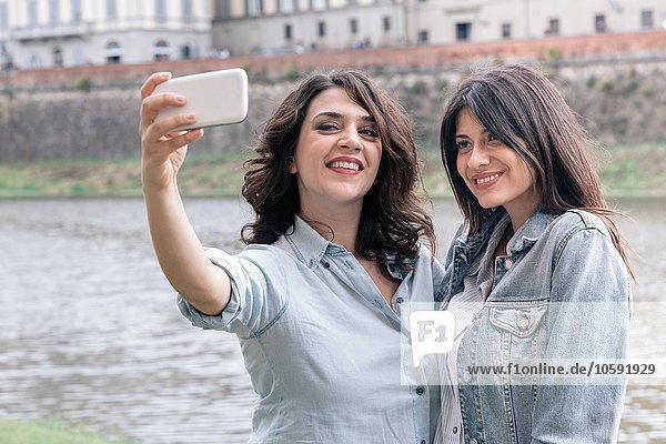 Lesbian couple using smartphone to take selfie next to Arno river  Florence  Tuscany  Italy