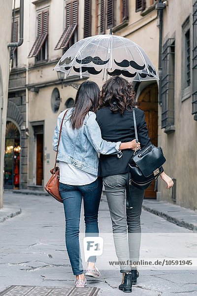 Rear view of lesbian couple walking together in street holding umbrella  Florence  Tuscany  Italy