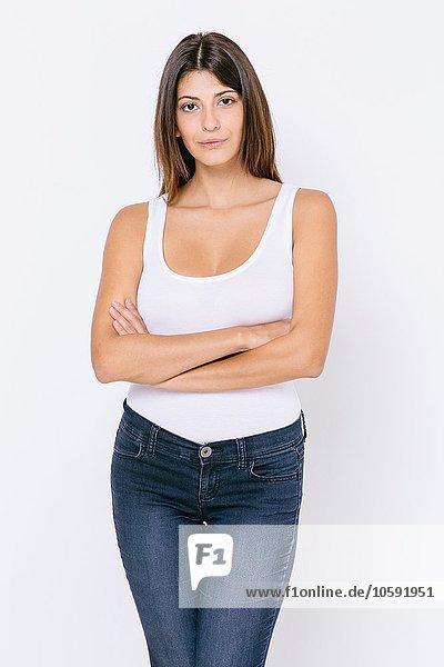 Young woman wearing white vest and skinny jeans arms crossed looking at camera