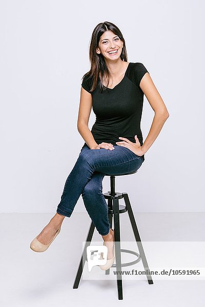Young woman sitting on stool looking at camera smiling