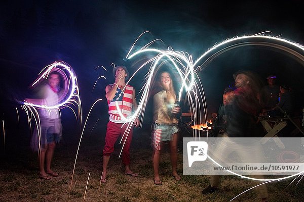 Four adult friends celebrating with sparklers in darkness on Independence Day  USA