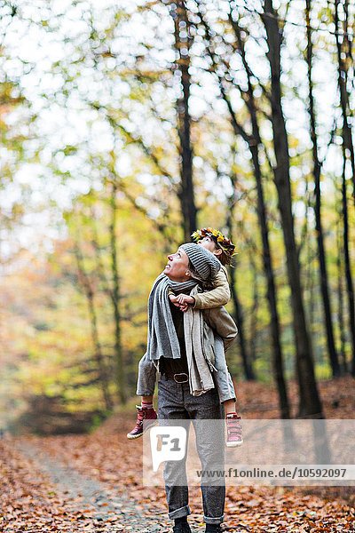 Mother giving daughter piggyback ride in autumn forest