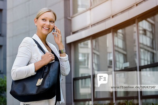 Young businesswoman talking on smartphone outside office