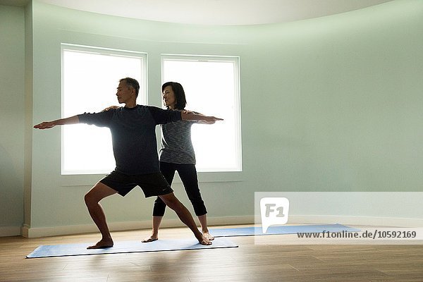 Vorderansicht des reifen Paares beim gemeinsamen Yoga  korrigierende Kriegerpose
