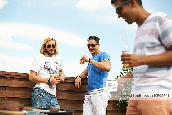 Drei männliche Freunde beim Biertrinken und Grillen auf dem Dach des Hauses