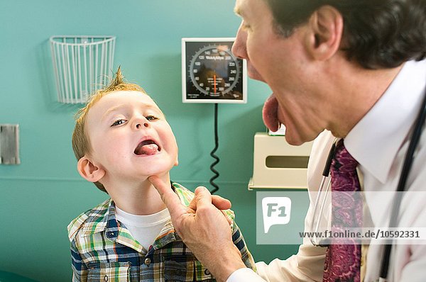 Männlicher Arzt mit Blick auf die Zunge des Jungen