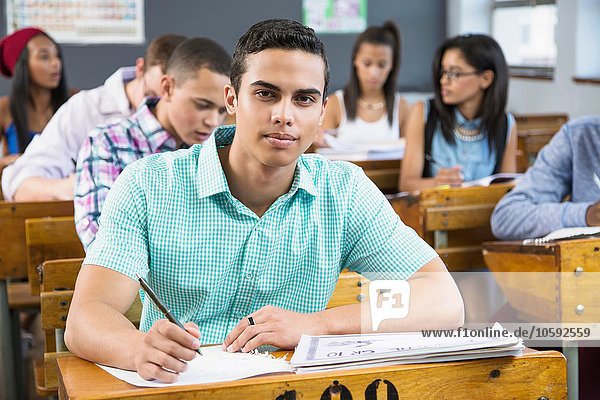 Porträt eines männlichen Schülers  sitzend am Schreibtisch im Klassenzimmer