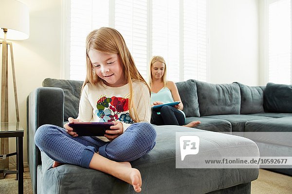 Mutter und Tochter mit digitalem Tablett auf dem Sofa im Wohnzimmer