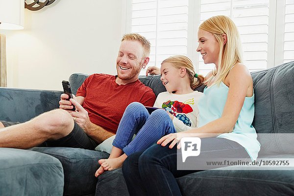 Family chatting and using smartphone on sofa in living room