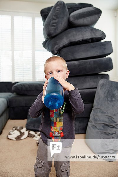 Junge trinkt im Wohnzimmer  Kissenstapel im Hintergrund